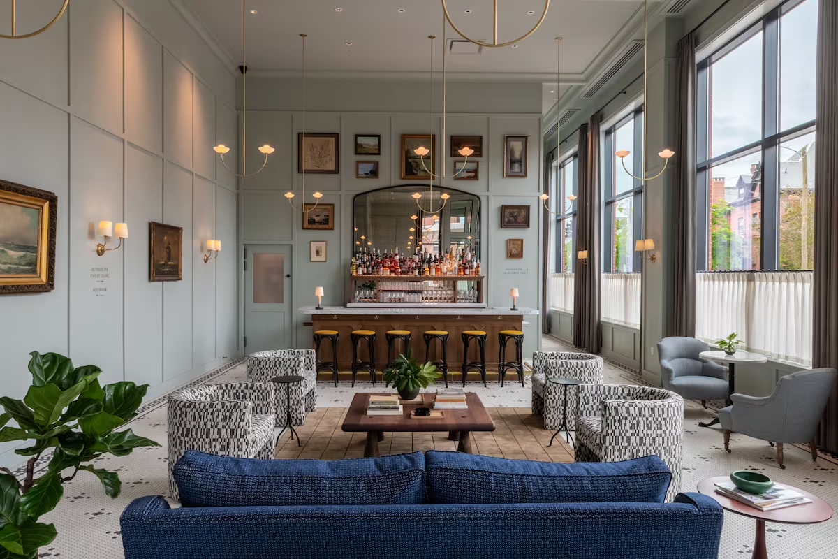 Salon d'hôtel élégant avec canapé bleu, fauteuils graphiques et bar au fond